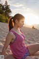 A woman in a pink tank top sitting on a sand dune.