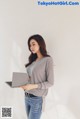 A woman standing in front of a white wall holding a laptop.