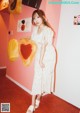 A woman standing in front of a pink wall holding a heart shaped pillow.