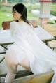 A woman in a white dress sitting on a wooden bench.