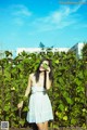 A woman in a white dress standing in front of a fence.