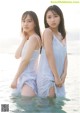 Two young women standing in the water wearing white dresses.