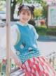 A young woman in a blue sweater and red and white skirt.